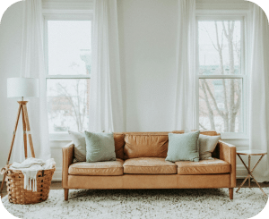 A white living room with a beige couch, elegant lamp, and sunlight streaming through the windows.